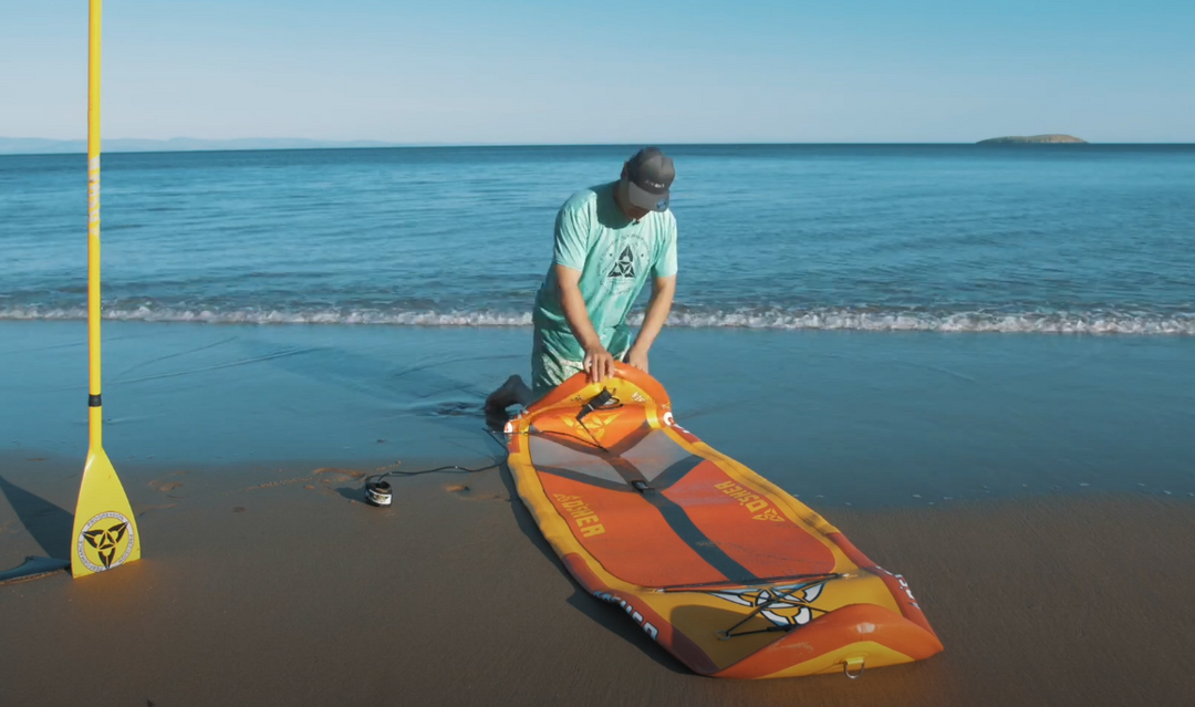 man on beach folding up SUP board